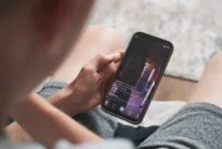 Caucasian teenager sits on sofa at home, surfs the Internet using mobile phone, spends leisure time. Social media feed with dancing young girl short video displayed on smartphone screen. Close Up.